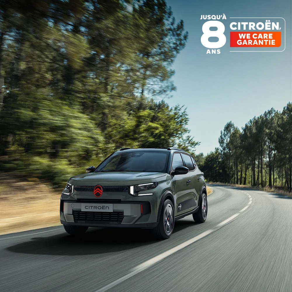 Vue avant trois quarts de la Citroën ë-C3 Outdoor avec signature lumineuse LED, mettant en avant le confort Citroën Advanced Comfort lors d’un trajet sur une route panoramique.