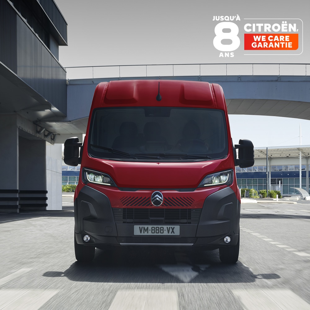 Vue de face d'un fourgon Citroën ë-Jumper rouge circulant dans un décor urbain moderne, mettant en avant son design robuste, son côté pratique et sa forte présence sur la route.