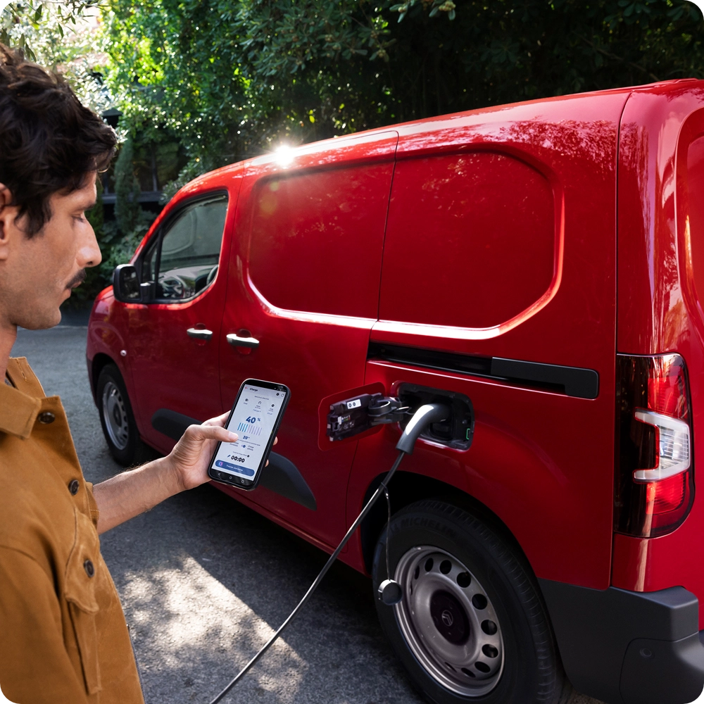 Vue de trois quarts latérale d’un Citroën ë-Berlingo Van en cours de recharge sur une borne publique, illustrant l’utilisation pratique de l’électrique, la connectivité et le confort au quotidien.