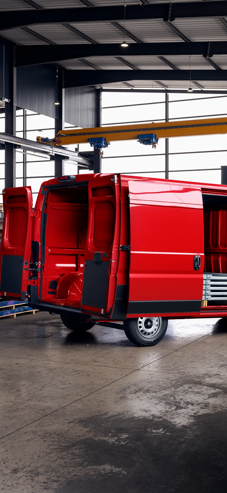 Vue arrière trois-quarts d'un Citroën ë-Jumper rouge avec les portes de chargement ouvertes à l'intérieur d'un entrepôt, mettant en avant le grand espace de chargement, la durabilité et la polyvalence professionnelle.