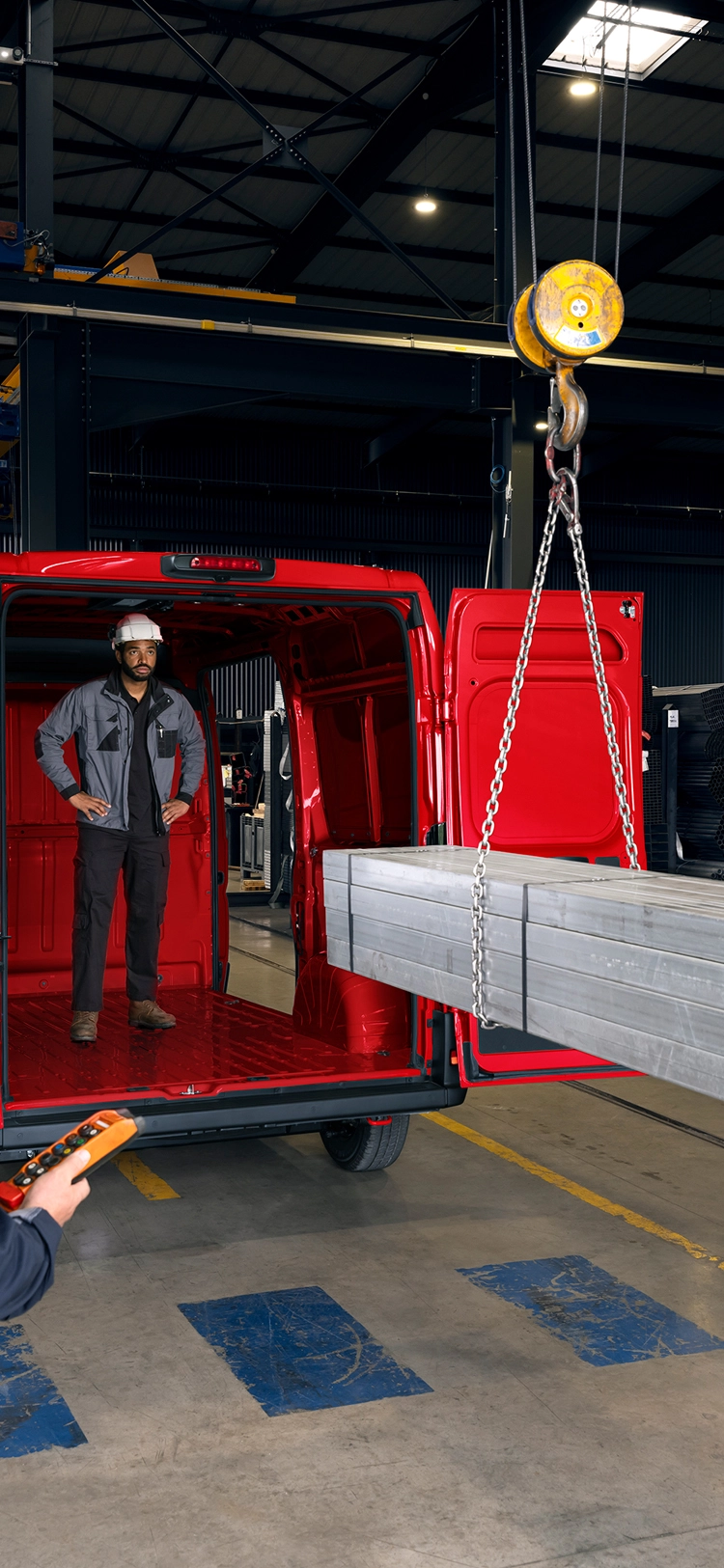 Vue arrière d'un Citroën ë-Jumper rouge en train d'être chargé de poutres métalliques dans un environnement industriel, mettant en avant le grand volume de chargement et la capacité à supporter de lourdes charges.