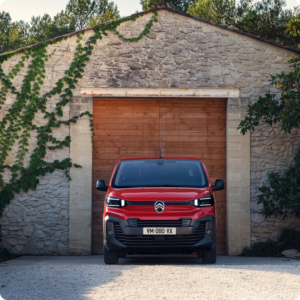 Vue extérieure avant d'une Citroën ë-Jumpy rouge garée devant un immeuble, mettant en avant son design professionnel, sa robustesse, son aspect pratique et sa présence imposante.