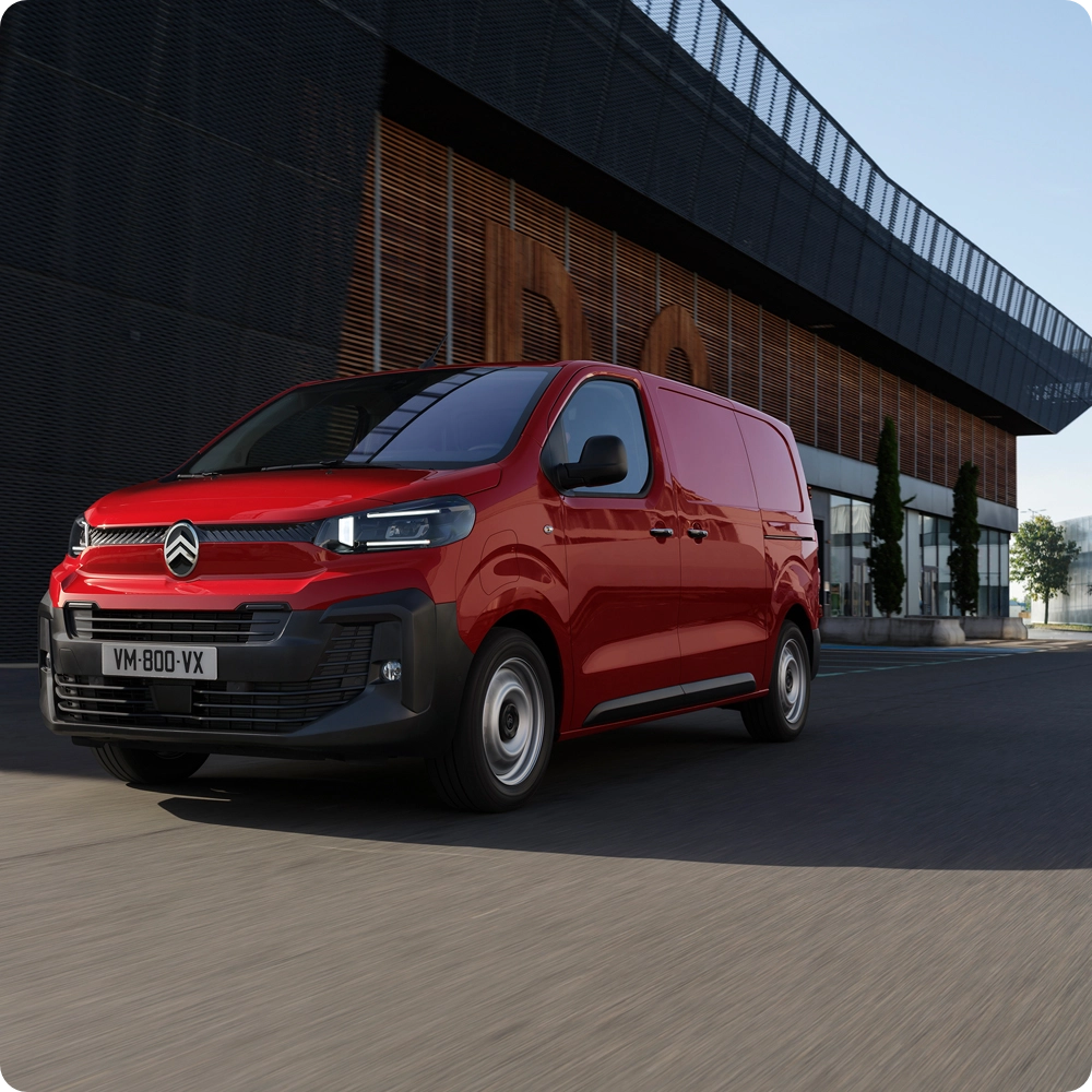 Vue de trois quarts avant d'un Citroën ë-Jumpy rouge circulant en milieu urbain, mettant en avant son design moderne, son confort de conduite, sa connectivité et son allure professionnelle et assurée.