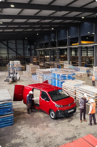 Vue extérieure en plongée d'une Citroën ë-Jumpy rouge garée dans un entrepôt industriel, mettant en avant ses dimensions extérieures compactes, sa grande capacité de chargement et son aspect pratique et professionnel.