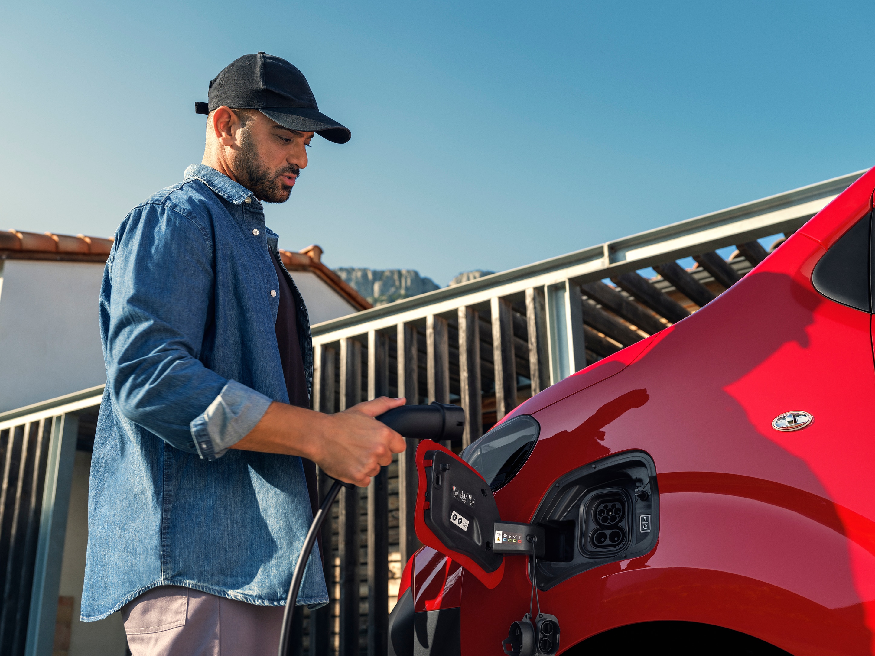 Vue extérieure de profil d'un Citroën ë-Jumpy rouge en cours de recharge à une borne, illustrant la facilité de recharge électrique, l'utilisation connectée et la mobilité professionnelle pratique.