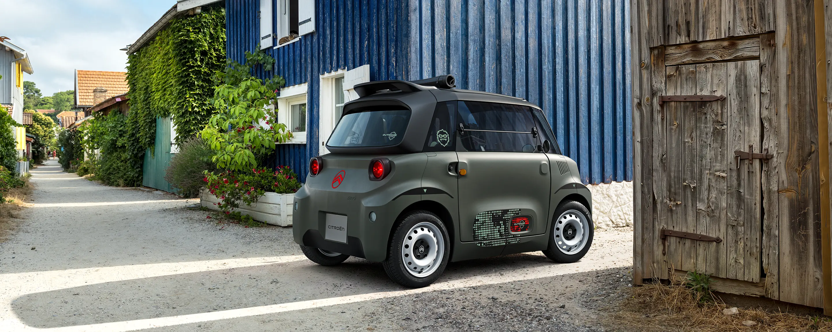 Vue avant trois-quarts de Citroën ami Outdoor avec phares LEDmontrant la voiture électrique urbaine compacte dans un village côtier