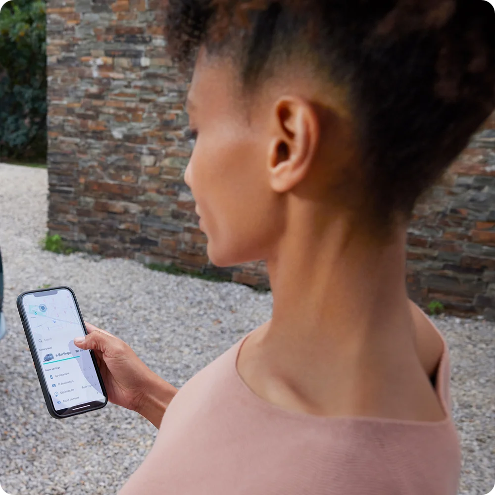 Personne utilisant un smartphone avec l'appli Free2Move Charge, mettant en avant la planification d'itinéraire fluide et le guidage vers les bornes de recharge pour la Citroën ë-C3 Van.