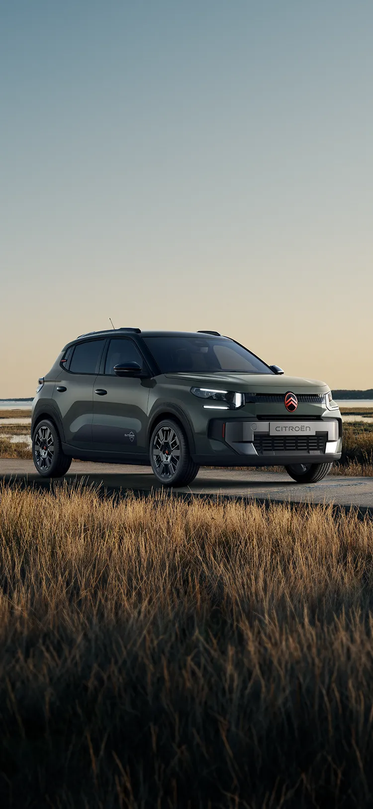 Vue avant trois quarts de la Citroën ë-C3 Outdoor avec signature lumineuse LED Advanced Comfort SUV, au bord de zones humides côtière