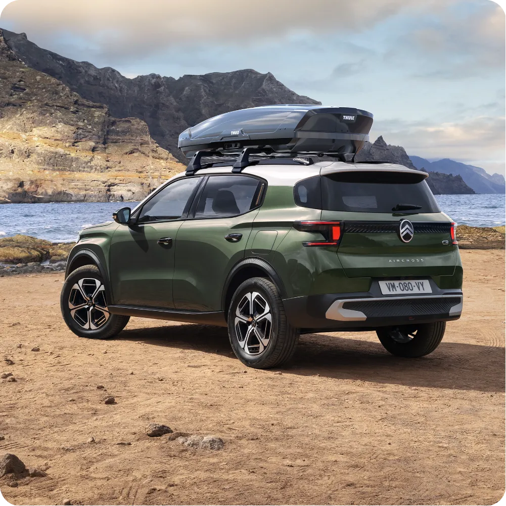 Vue extérieure du SUV Citroën ë-C3 Aircross équipé de barres de toit et d’un coffre de toit, mettant en avant sa polyvalence, son espace de chargement et ses capacités de voyage accessibles pour toutes les aventures. 