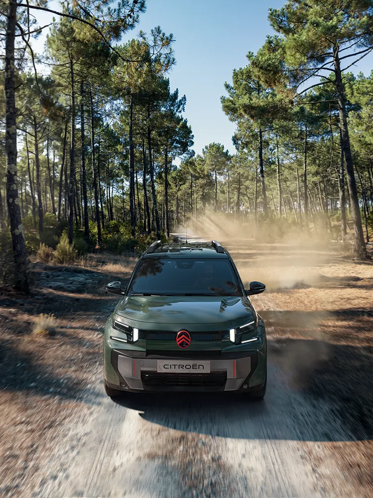 Vue aérienne avant du SUV Citroën ë-C3 Aircross OUTDOOR, mettant en valeur sa signature lumineuse LED, le programme Advanced Comfort et son esprit de SUV familial sur un chemin forestier.