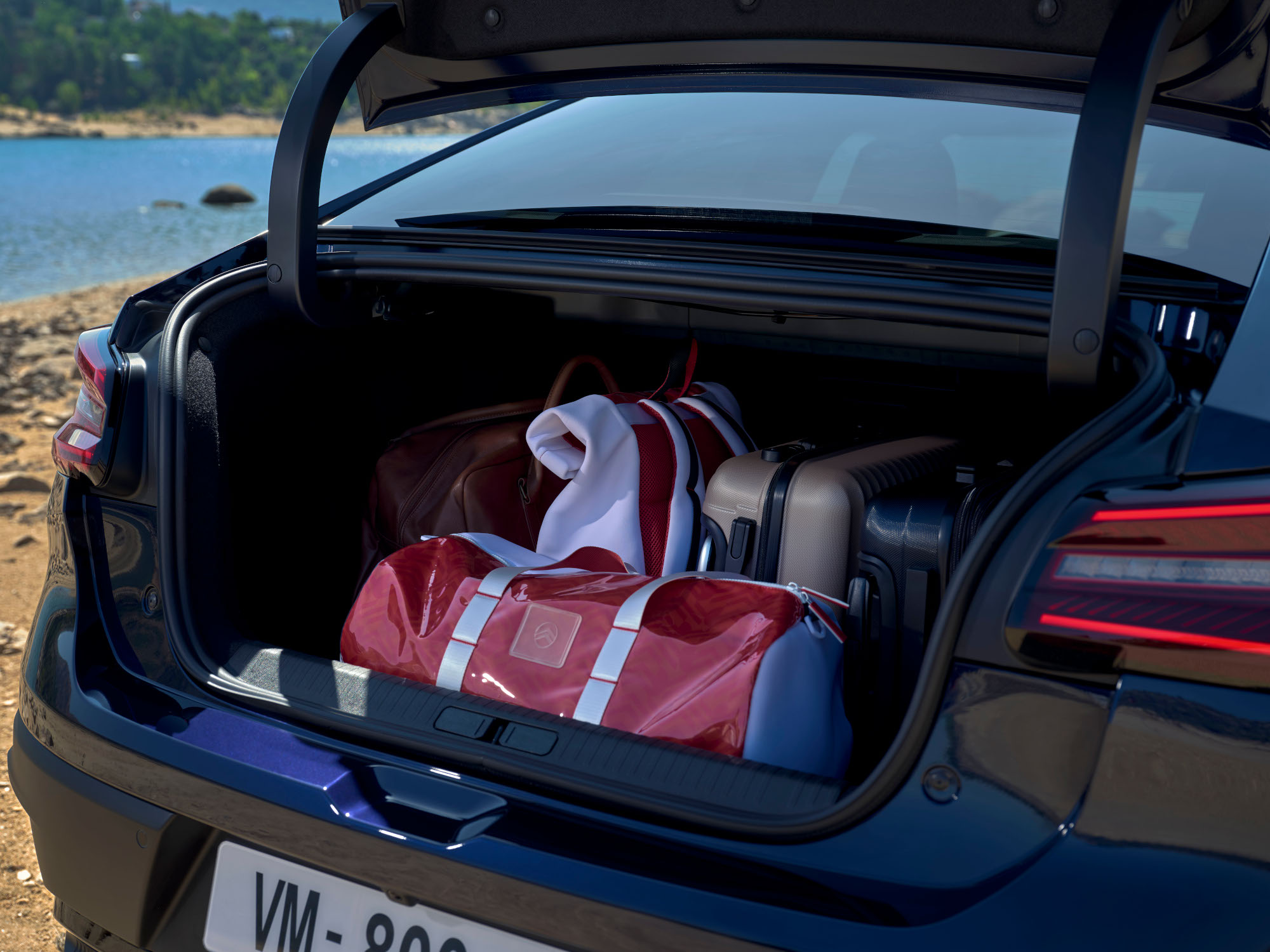 Coffre ouvert de la Citroën ë‑C4 X chargé de sacs de voyage au bord d'un lac