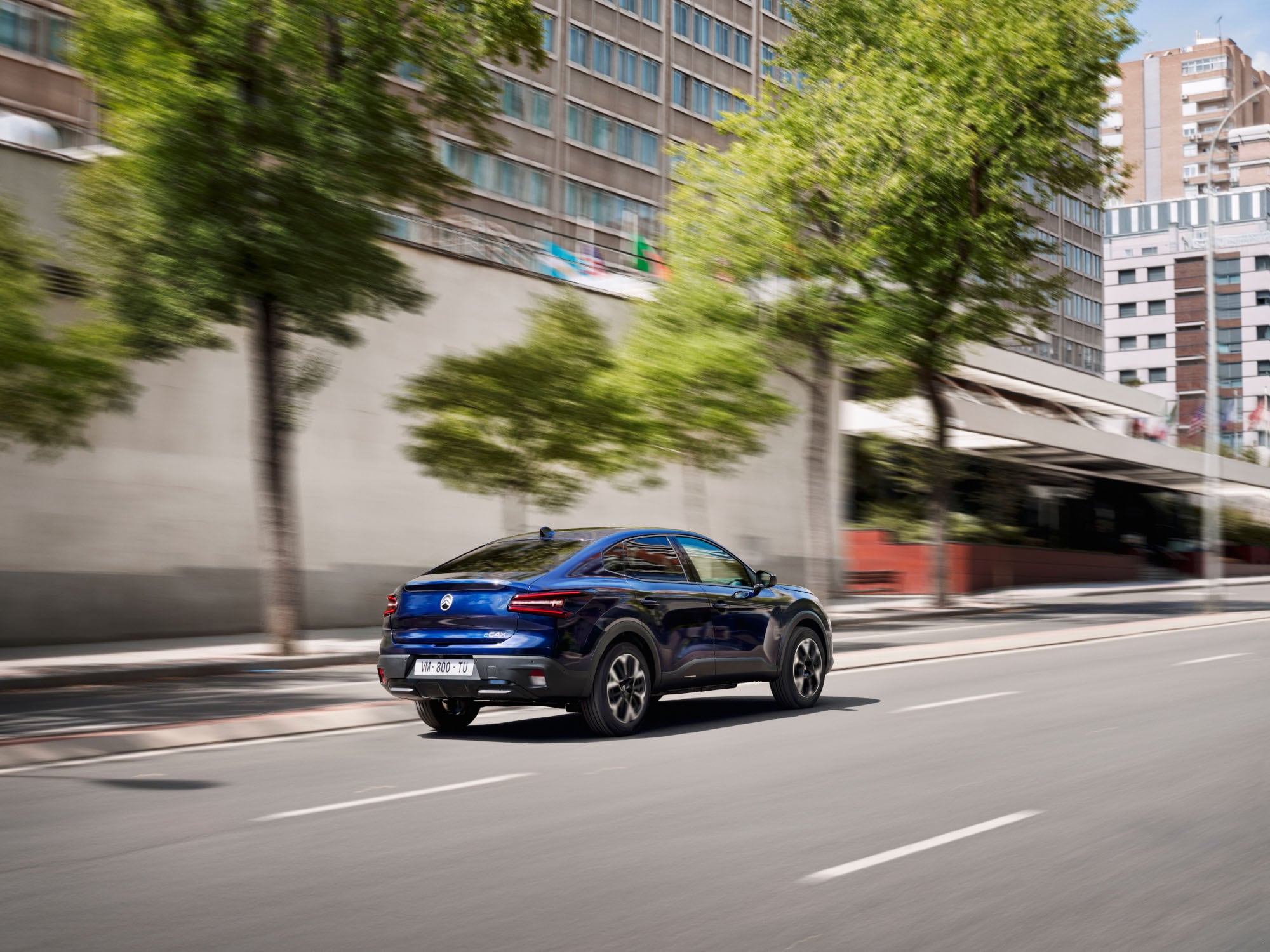 Vue 3/4 arrière de la Citroën ë-C4 X en mouvement, avec son style fastback mobilité abordable