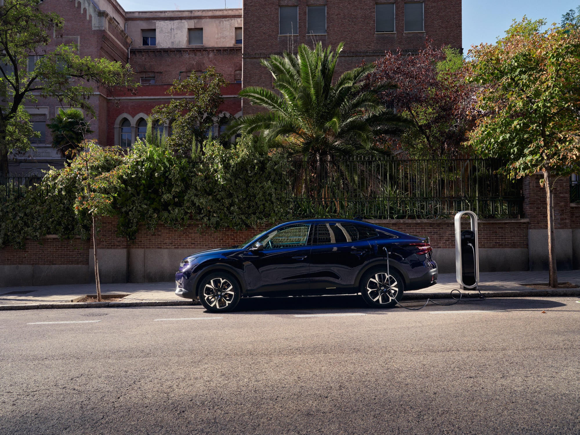 Vue côté de la Citroën ë-C4 X élec. fastback en cours de recharge dans la rue, avec une mobilité urbaine pratique